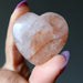 Heart-shaped quartz stone held between fingers against a dark background