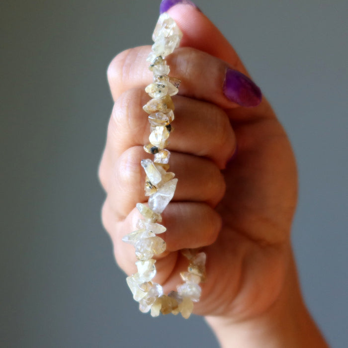 Hand holding a Rutilated Quartz bracelet made of small stones against a neutral background