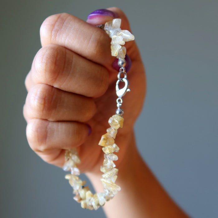 Hand holding a beaded Rutilated Quartz bracelet against a neutral background