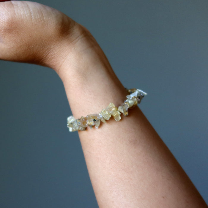 Rutilated Quartz bracelet with stones on a wrist against a gray background