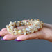 Hand holding a beaded Rutilated & Clear Quartz bracelet against a gray background
