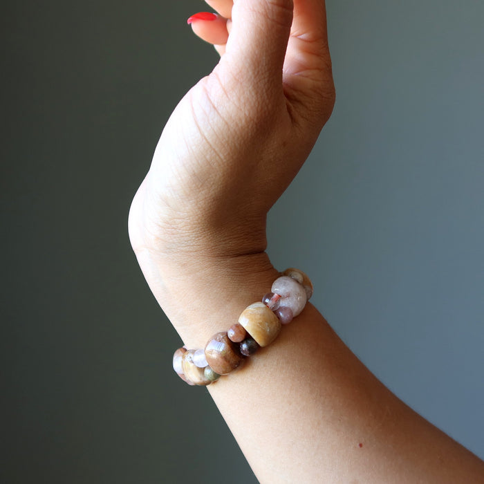Hand wearing a beaded bracelet against a neutral background