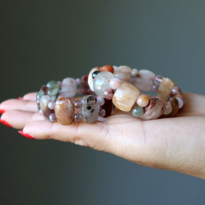 Hand holding a stack of multicolored beaded bracelets against a dark background