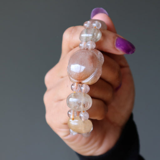 Hand holding a bracelet with clear and beige beads against a gray background