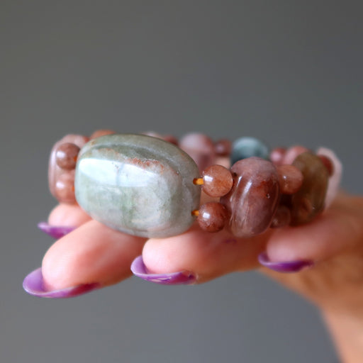 Hand holding a bracelet with multicolored beads against a gray background