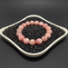 Pink rhodochrosite bracelet on a bed of black rice in a white dish against a dark background