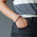Person wearing a pink beaded bracelet on a gray background