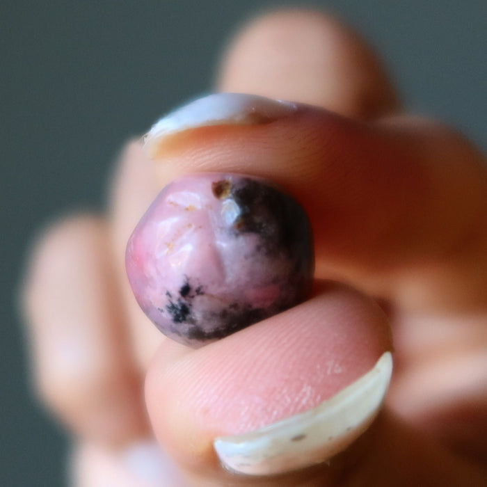 Hand holding a pink and black Rhodonite apple stone