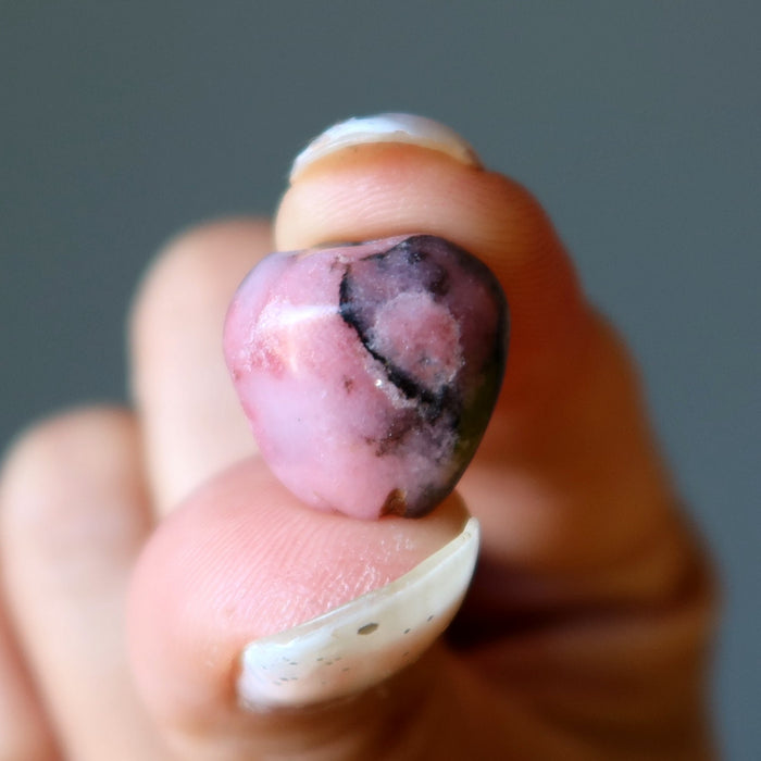 Hand holding a pink and purple Rhodonite apple stone against a blurred background