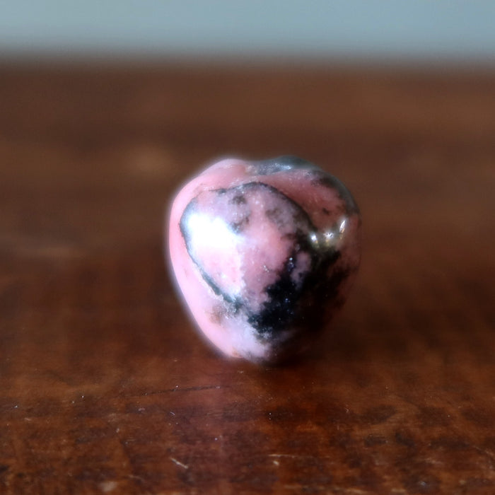 Heart-shaped pink Rhodonite apple stone on a wooden surface