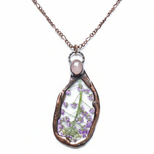 Teardrop-shaped pendant with pressed flowers and a rose quartz stone on a white background