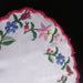 Embroidered floral design on a white fabric with a red scalloped edge against a dark background