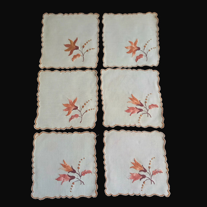 Set of six brown embroidered doilies from Hungary with floral designs on a dark surface.