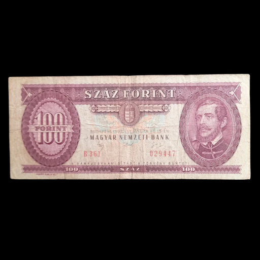A vintage Hungarian 100 Forint banknote from the Magyar Nemzeti Bank, featuring a portrait on the right and serial numbers on the left, displayed on a dark textured background.