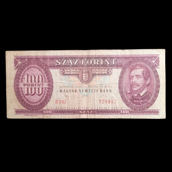 A vintage Hungarian 100 Forint banknote from the Magyar Nemzeti Bank, featuring a portrait on the right and serial numbers on the left, displayed on a dark textured background.