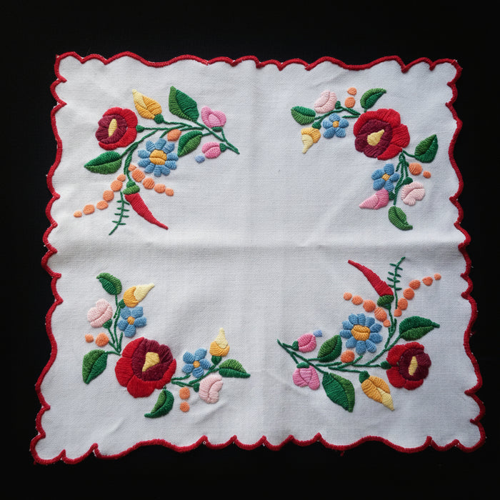 Embroidered floral kalocsa hungarian design on a white fabric with red scalloped edges against a dark background