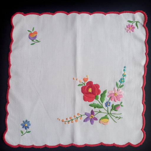 White hungarian kalocsa doily table topper with colorful floral embroidery on a dark background