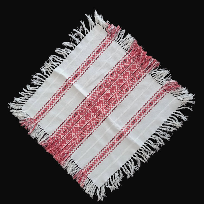 White fabric with red patterns and fringes handmade Hungarian table topper on black background