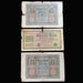 Three vintage German banknotes laid flat on a dark fabric background, arranged vertically. The top note is a Burdert Mark, the middle is a 1000 Mark note, and the bottom is a larger Mark note.