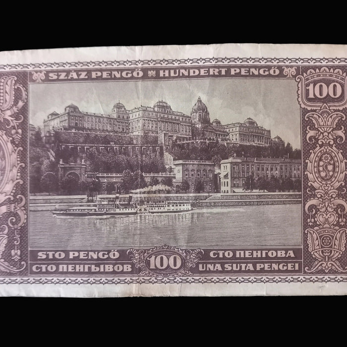 A vintage Hungarian 100 Pengó banknote featuring a sepia-toned illustration of the Buda Castle and Danube River, photographed flat against a dark background.