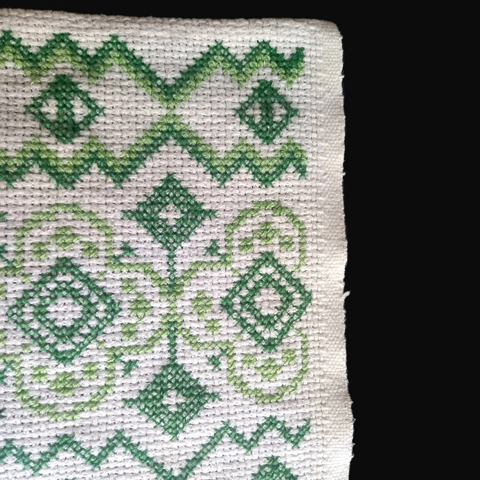 Close-up of cross-stitched green pattern on white fabric with a black border. hungarian folk art