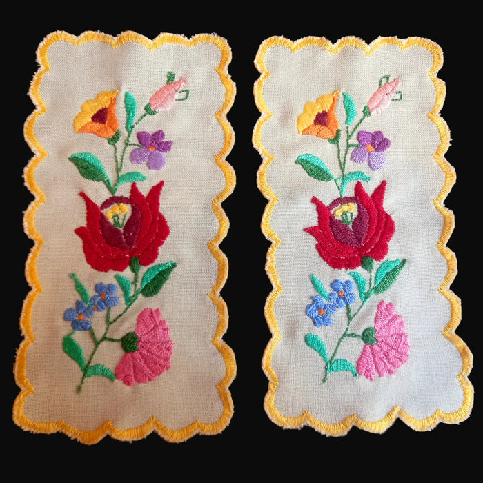Two Hungarian Kalocsa embroidered floral designs on a beige linen with yellow scalloped edges.
