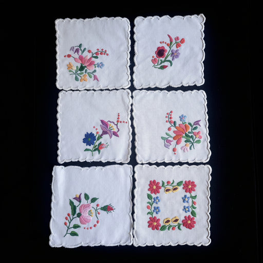 Set of six embroidered floral hungarian kalocsa napkin doilies on a dark surface