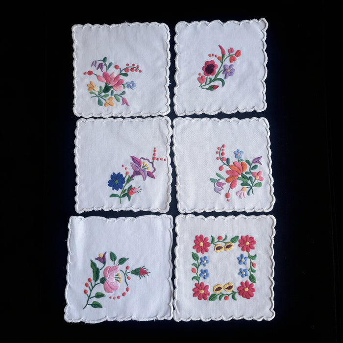 Set of six embroidered floral hungarian kalocsa napkin doilies on a dark surface