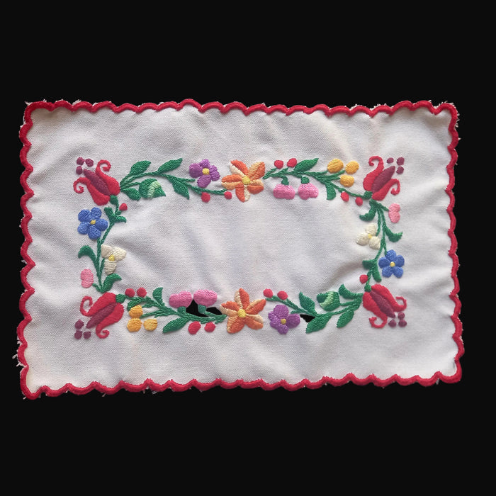 Embroidered floral design on a white fabric with a red border against a black background. hungarian folk art kalocsai