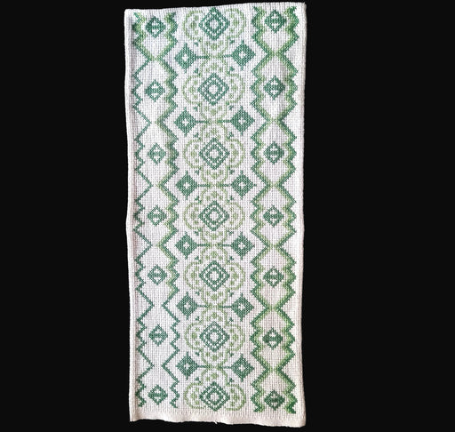 Cross-stitched green pattern on white fabric from Hungary, against a dark background