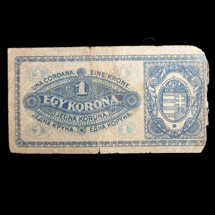 A vintage 1 Corona banknote from Hungary, printed in blue ink on aged, yellowed paper, displayed flat against a dark textured fabric background.