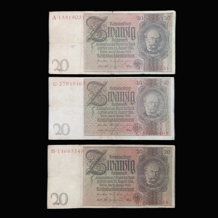 Three vintage German 20 Reichsmark banknotes are arranged vertically on a dark fabric background. Each note shows the portrait of Wilhelm Gustloff, serial numbers on the left, and ornate printed details in faded beige, brown, and gray tones.