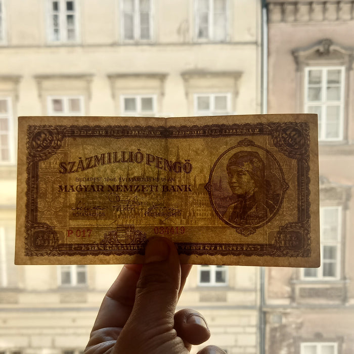 Hand holding an old hungarian pengo 100 million banknote with a blurred building in the background