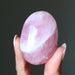 Hand holding a pink rose quartz crystal against a dark background