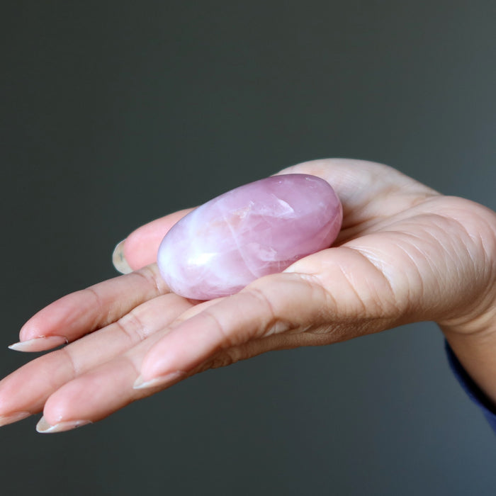 Hand holding a pink rose quartz crystal against a dark background