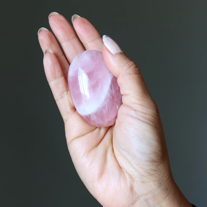 Hand holding a pink rose quartz crystal against a dark background