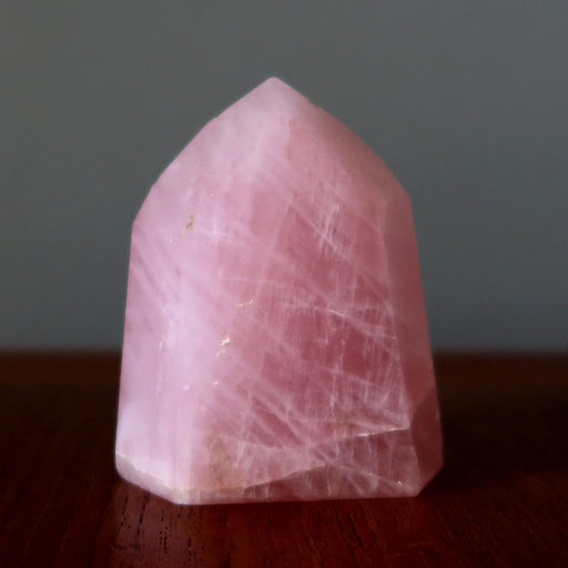 Pink  rose quartz crystal on a dark surface with a neutral background