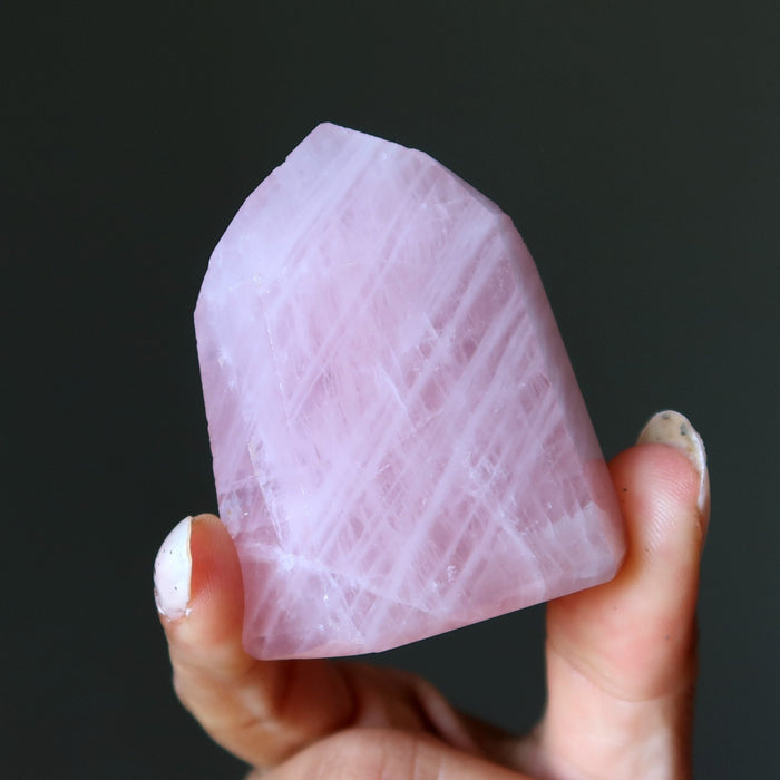 Hand holding a pink rose quartz  crystal against a black background