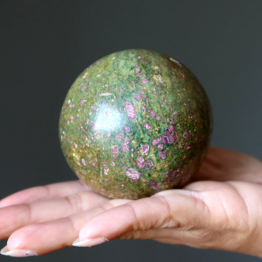 Hand holding a green and pink ruby fuchsite stone against a dark background