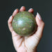 Hand holding a green ruby fuchsite stone ball against a dark background