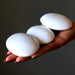Hand holding three white Scolecite stones against a dark background