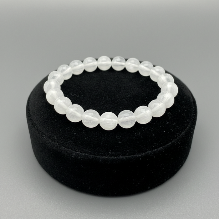 White selenite beaded bracelet on a black velvet stand with a gray background
