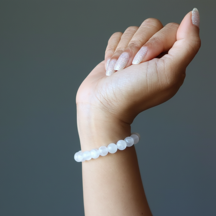 Hand wearing a white selenite beaded bracelet on a gray background