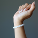 Hand wearing a white selenite beaded bracelet on a gray background