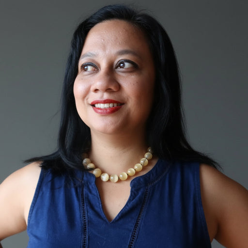 Woman wearing a blue sleeveless top and selenite necklace against a gray background