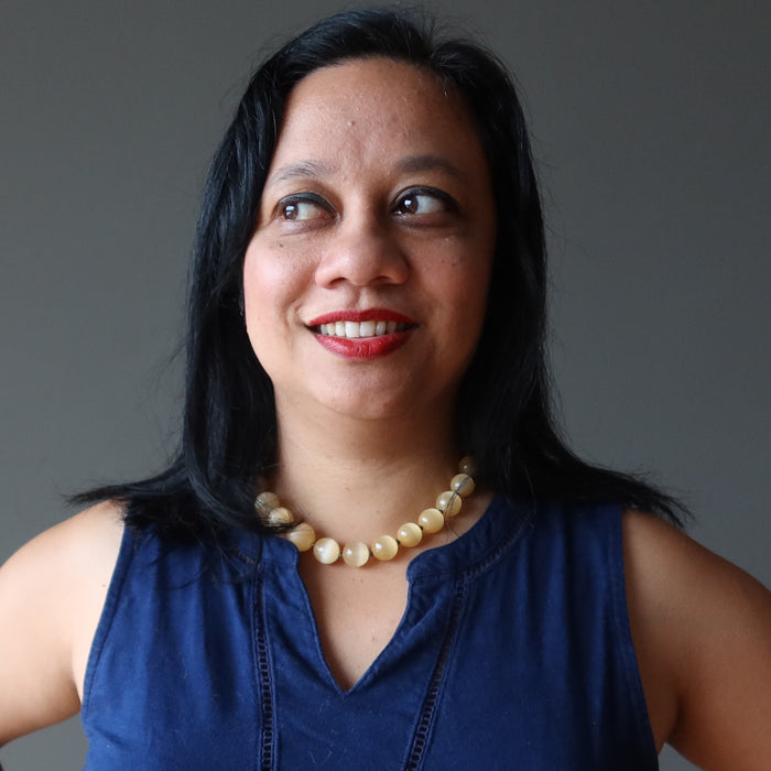 Woman wearing a blue sleeveless top and selenite necklace against a gray background