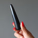 Hand holding a black Shungite massage wand against a gray background