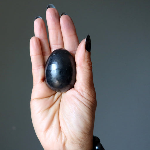 Hand holding a shungite egg stone against a gray background
