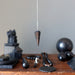Black Shungite pendulum and other black objects on a wooden surface with a neutral background