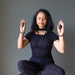 Woman in a meditative pose holding black Shungite stones against a gray background